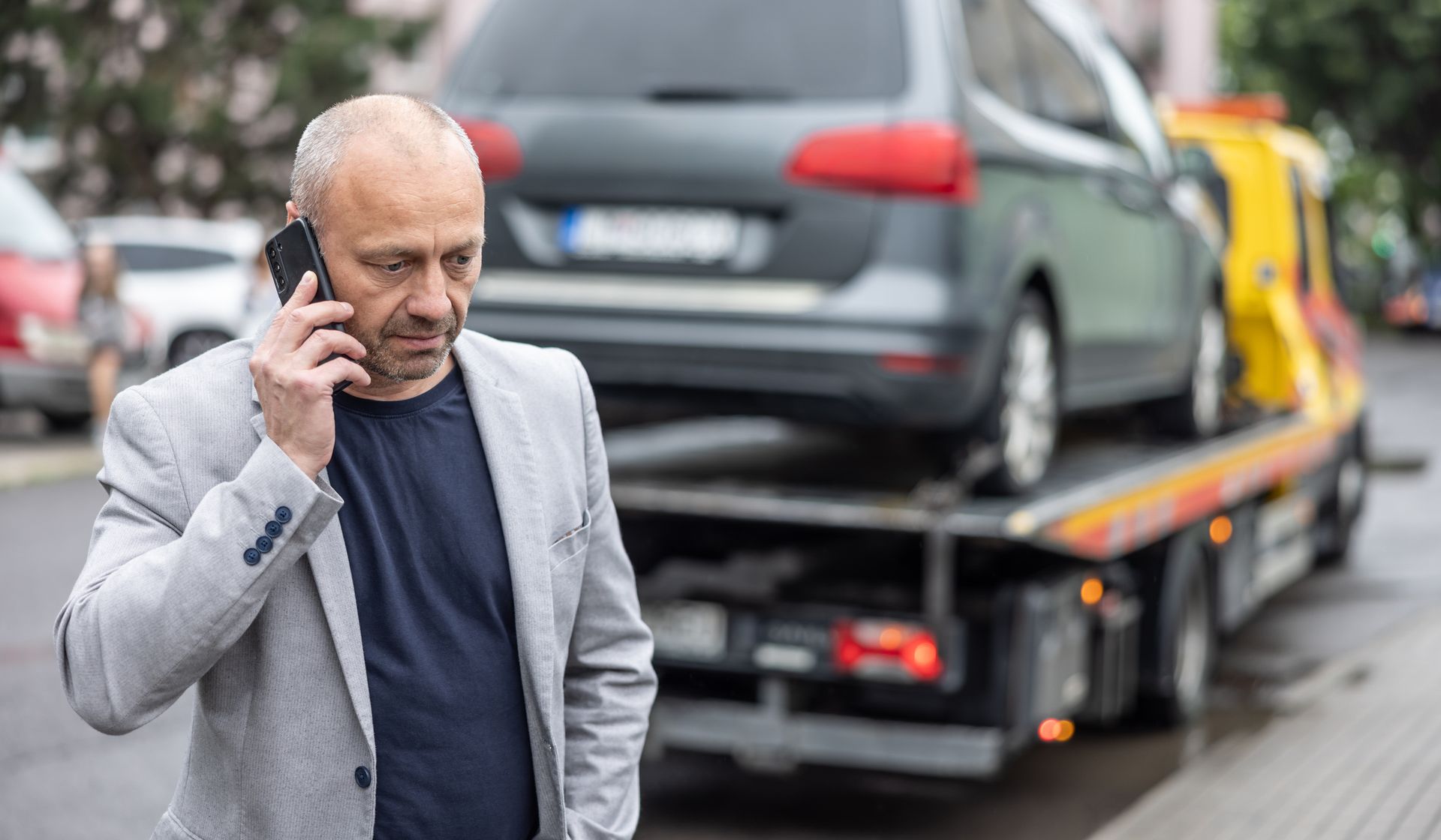 Elegant middle-aged businessman speaking on the phone while towing service helping his on the road. Elegant middle-aged businessman speaking on the phone while towing service helping his on the road.