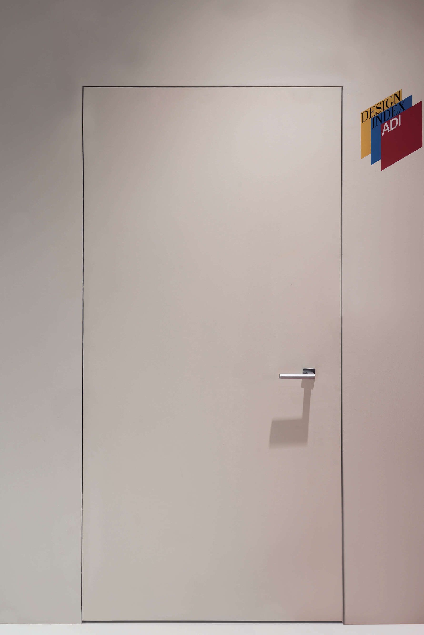 Porta beige con maniglia argentata e insegne colorate su una parete bianca.