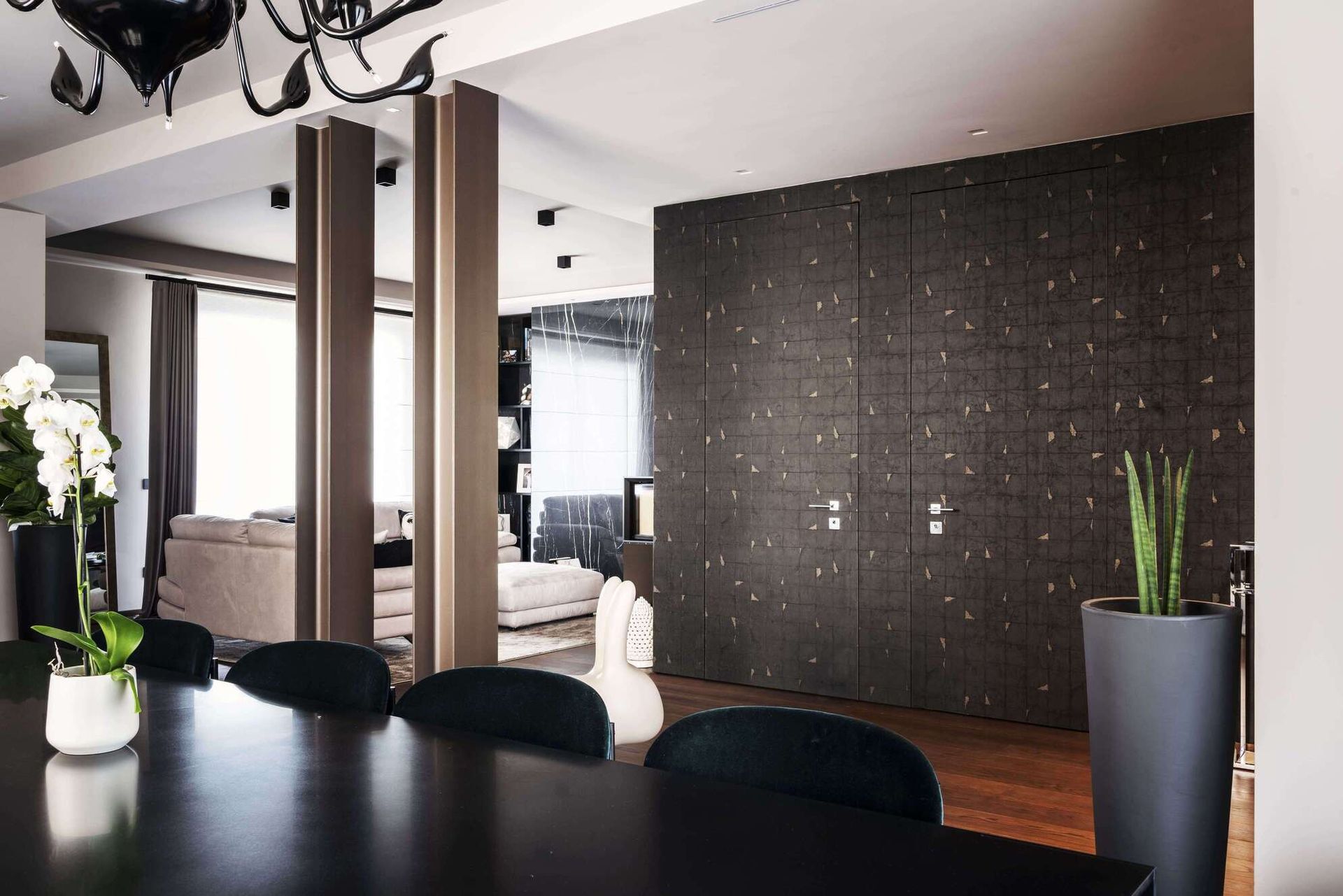 Moderna sala da pranzo con tavolo nero, sedie e parete scura con pianta.