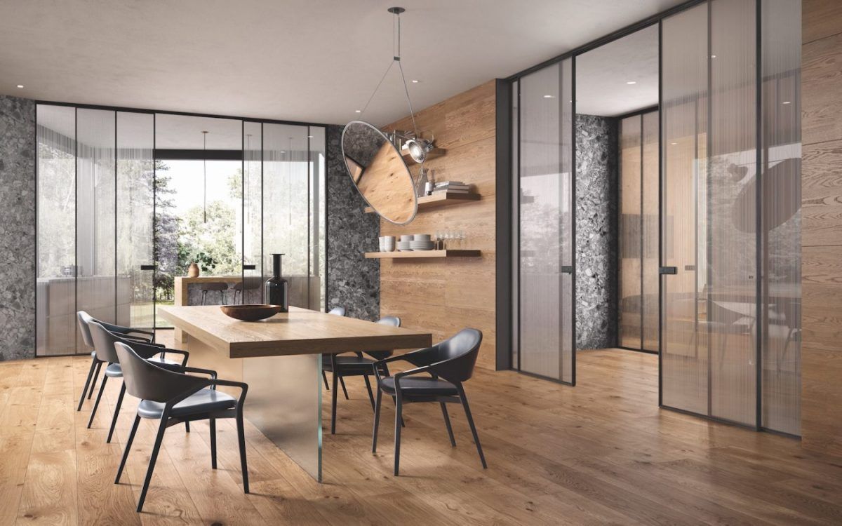 Sala da pranzo con tavolo in legno, sedie nere, pareti in vetro e parete decorativa in pietra.