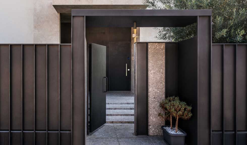 Un cancello e una porta in metallo scuro conducono all'ingresso di una casa moderna.