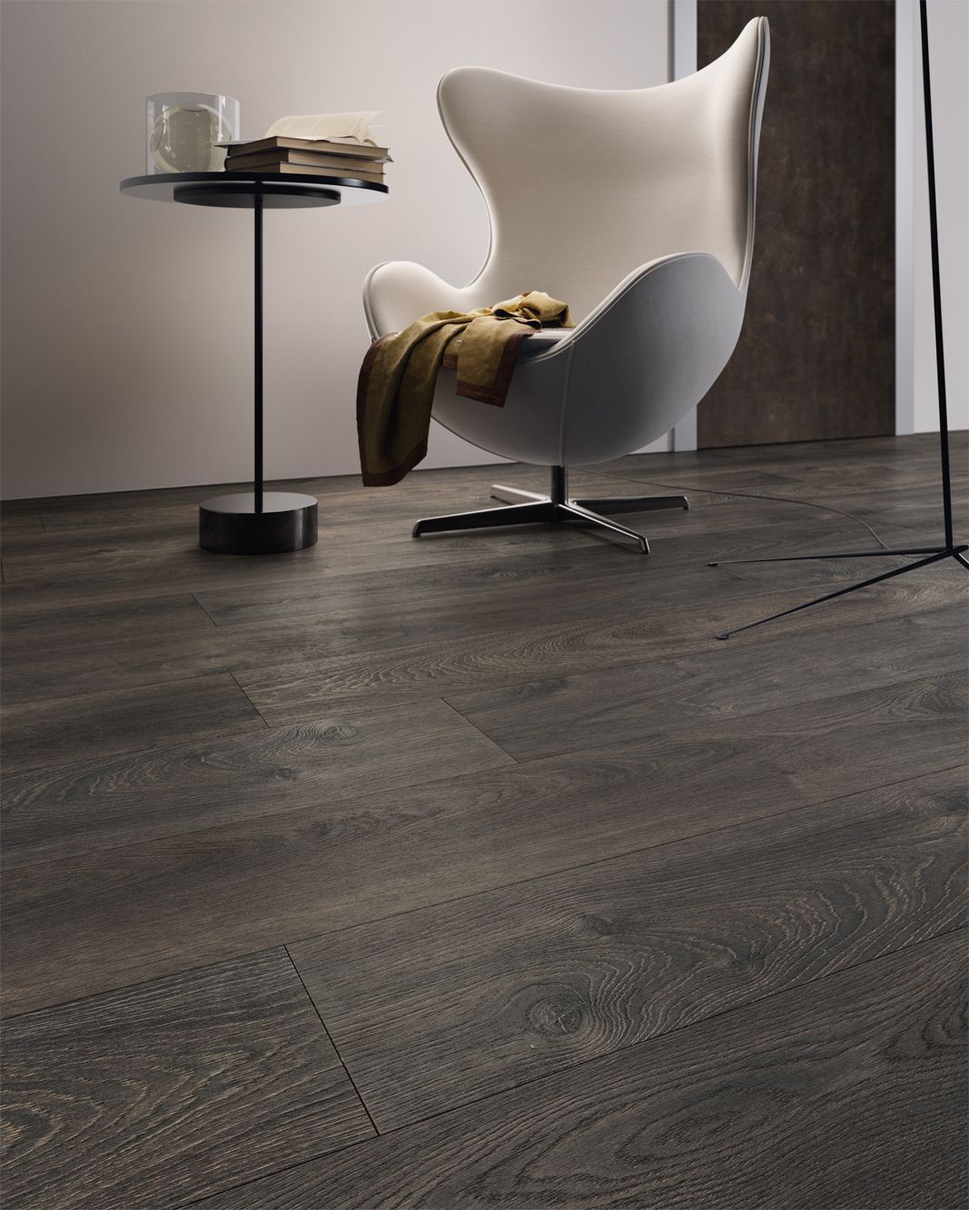 Pavimento in legno scuro in una stanza con una moderna sedia bianca, un tavolino e una coperta.