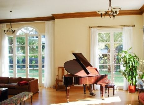 Pianoforte a coda in un soggiorno soleggiato con ampie finestre, pareti color crema e finiture in legno.