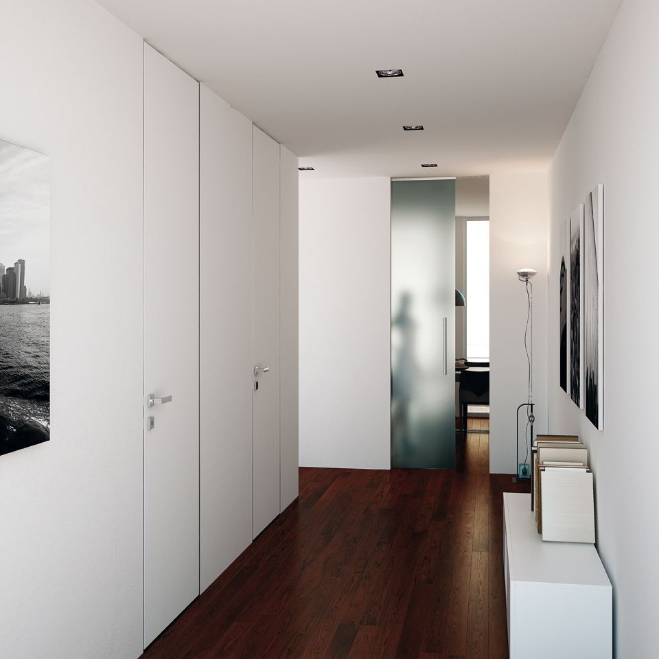 Corridoio con pareti bianche, armadi a muro, pavimento in legno scuro, porta scorrevole in vetro smerigliato e opere d'arte.