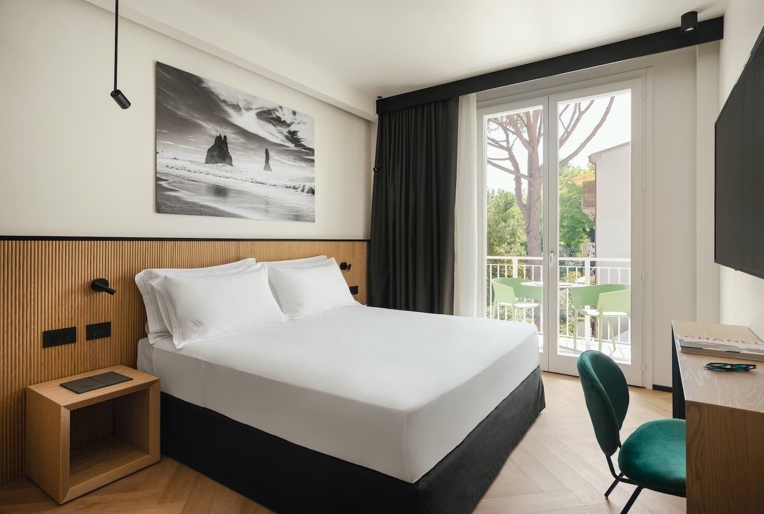 Camera d'albergo con letto, scrivania e balcone con vista sugli alberi.