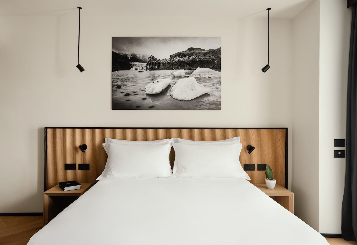 Camera da letto con letto bianco, testiera in legno e quadri paesaggistici in bianco e nero.