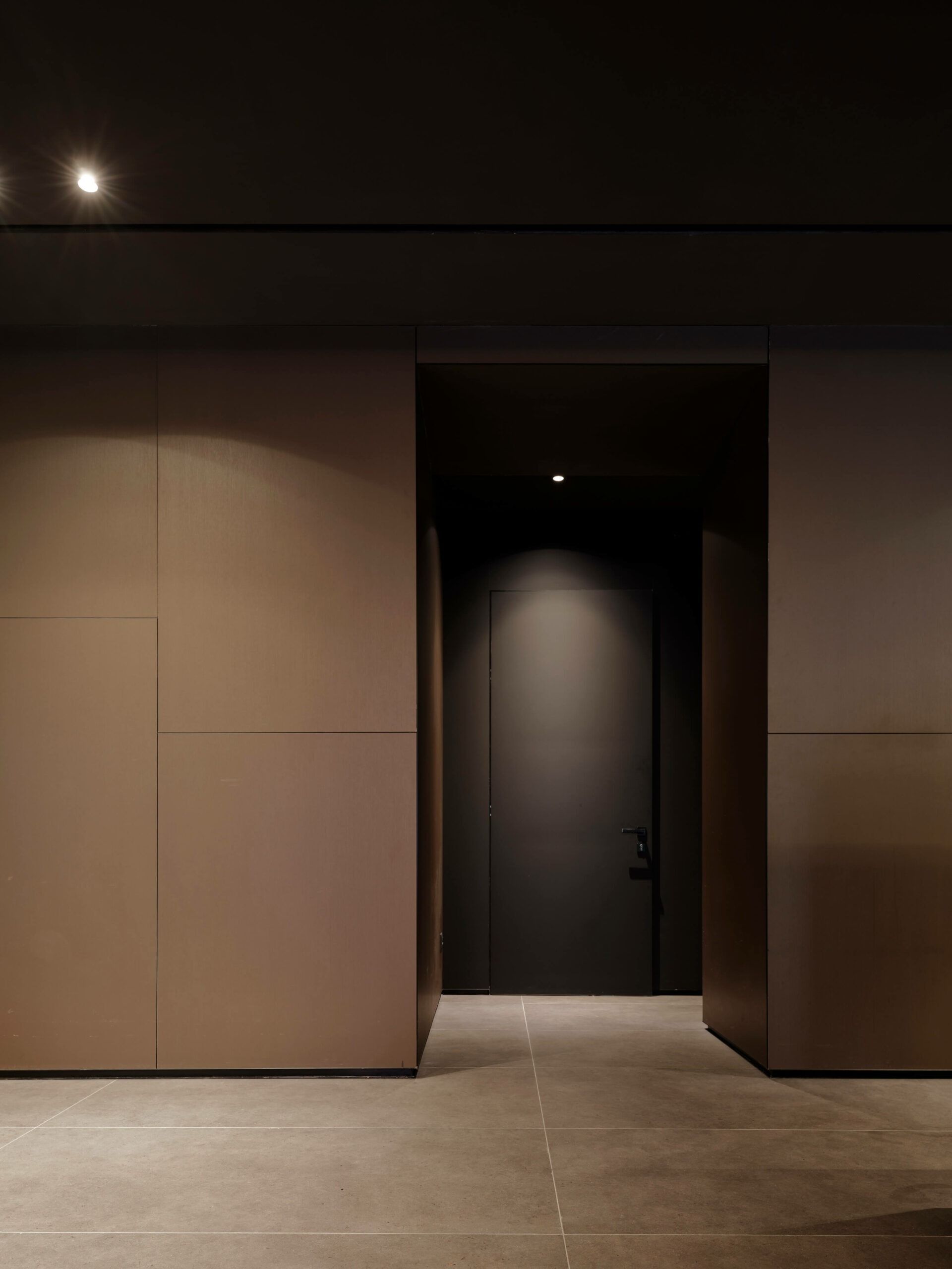 Corridoio buio con una porta e una porta chiusa in fondo. Pareti beige e soffitto scuro.