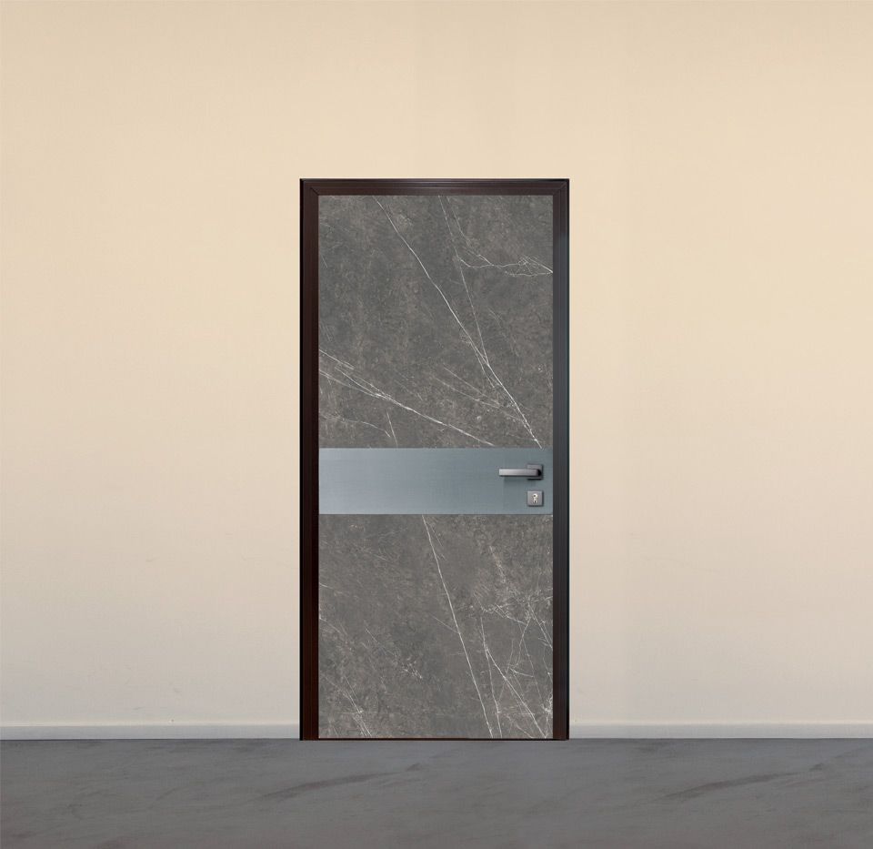Porta grigia testurizzata con barra decorativa argentata e cornice marrone scuro contro una parete beige.