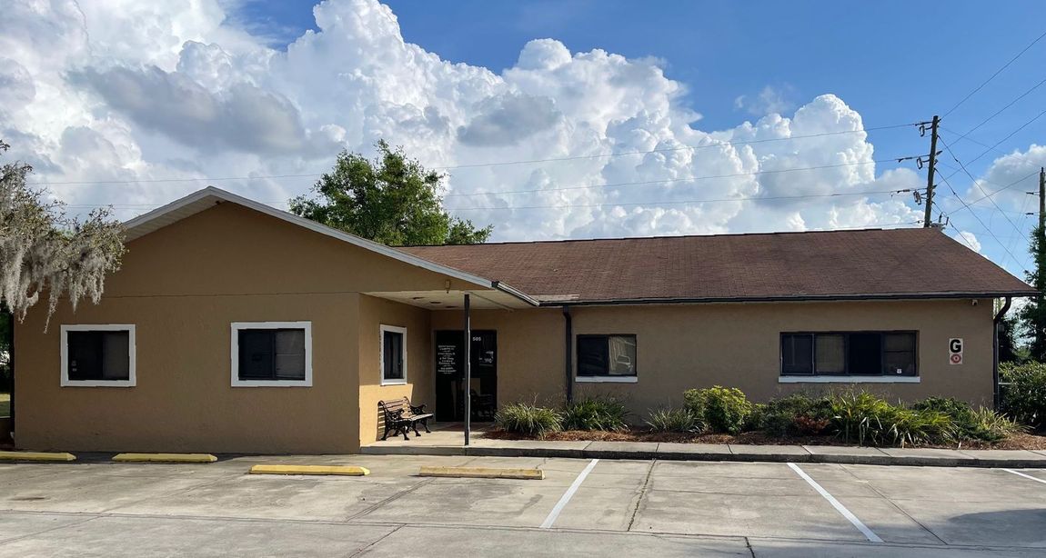 Tan single-story commercial building with a brown roof and small windows, under a cloudy sky.