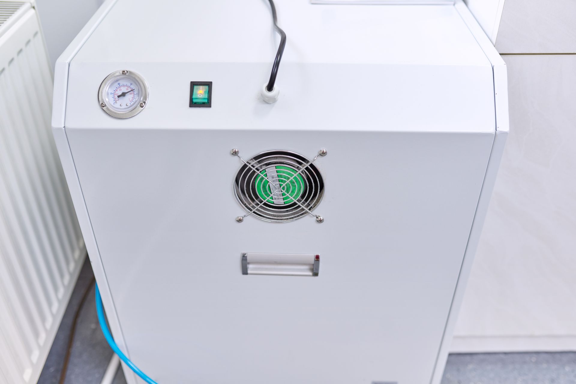 White industrial machine with gauge, switch, fan vent, and handle in a bright room