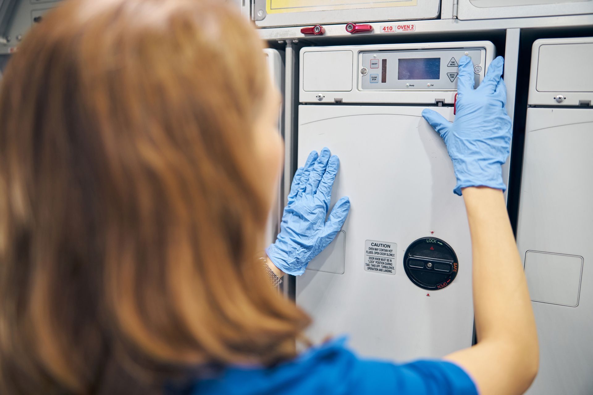 Technician in blue gloves adjusting controls on a lab machine in a clinical setting