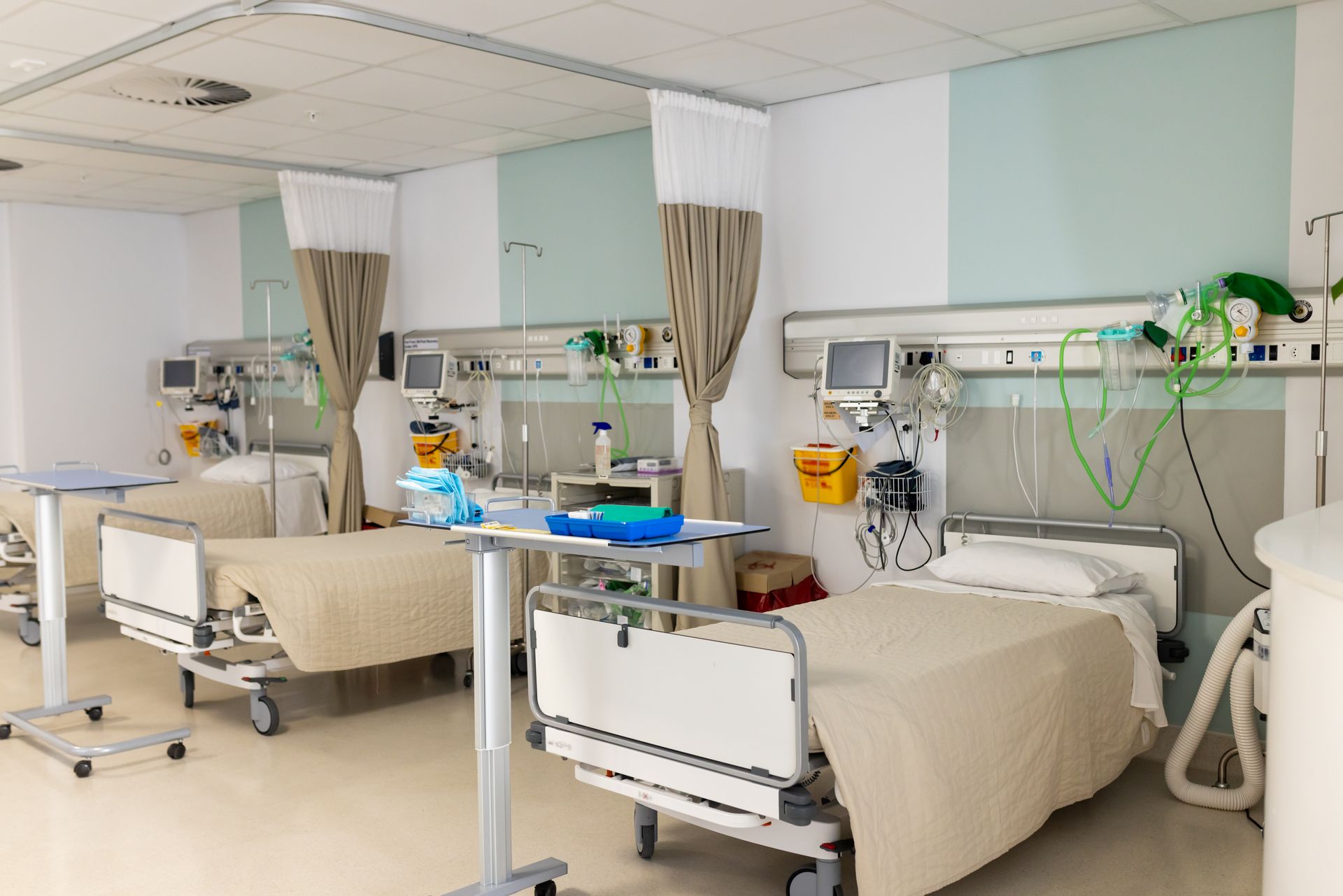 Hospital room with two beds, medical monitors, IV poles, and privacy curtains