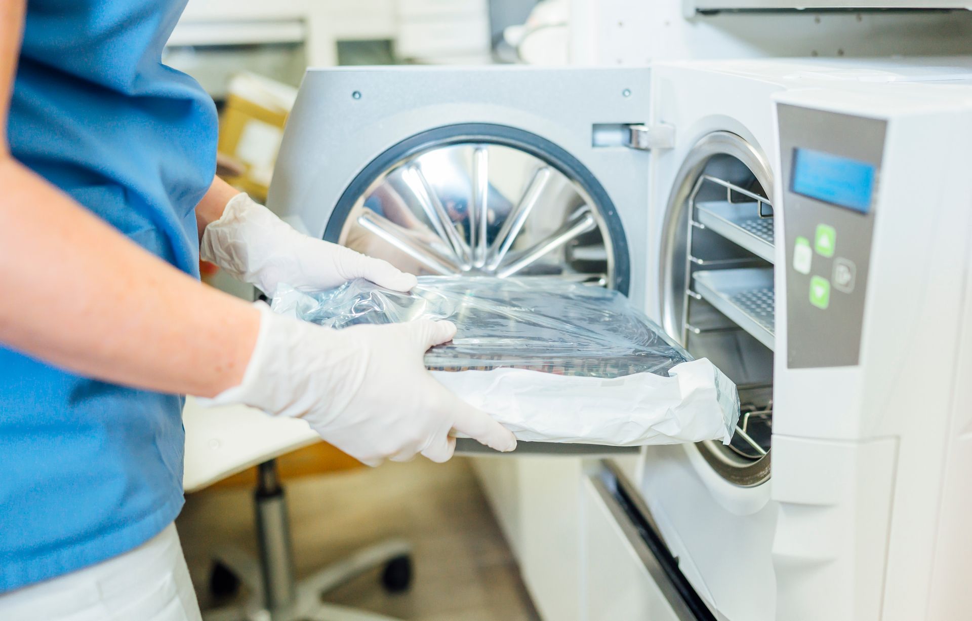 Gloved worker loading a wrapped tray into an open sterilizer or washing machine
