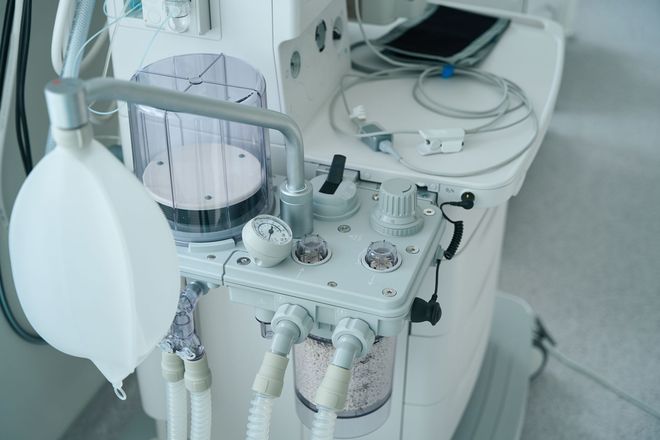 Close-up of a hospital anesthesia machine with gauges, tubing, and a breathing mask in a clinical room