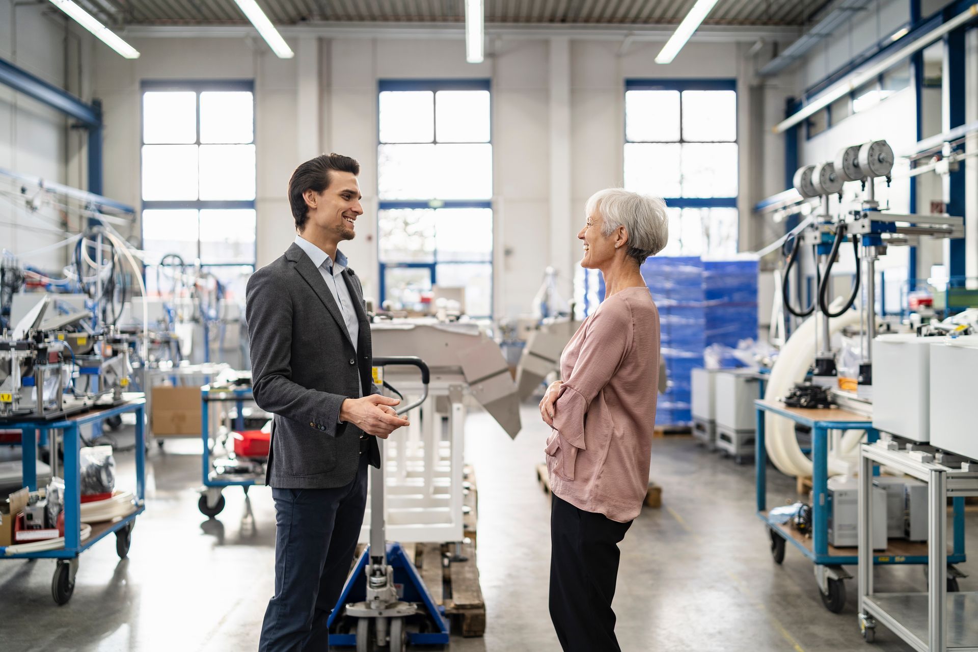 Two people talking in a bright factory workshop beside machinery and workstations