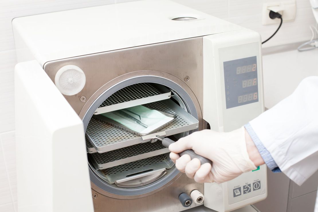 Hand placing a tray into a sterilizer or autoclave with the door open