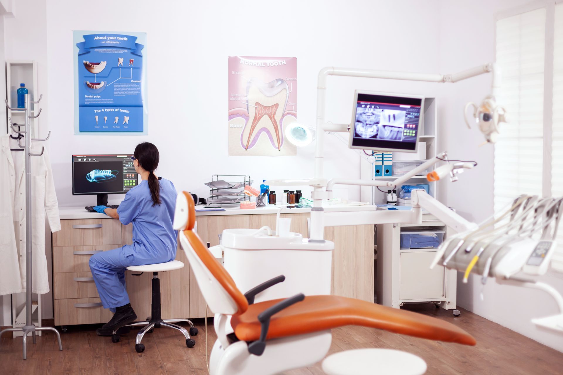 Dental clinic with dentist at computer, patient chair, and exam monitor in a bright treatment room