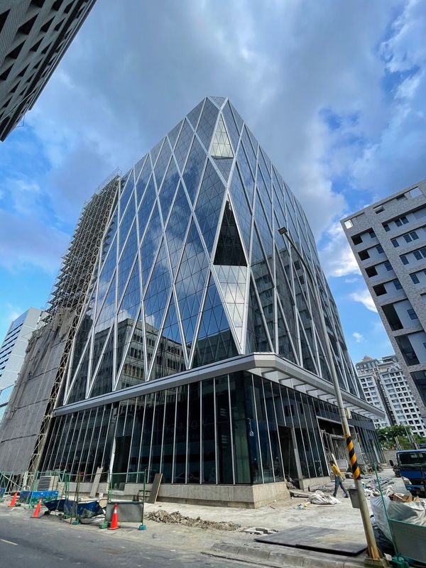 現代玻璃建築，菱形立面映襯著陰雲密佈的天空。地面上可見建築材料。