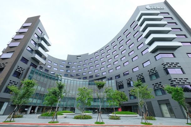 現代灰色飯店建築，外觀呈弧形，門前綠樹成蔭。