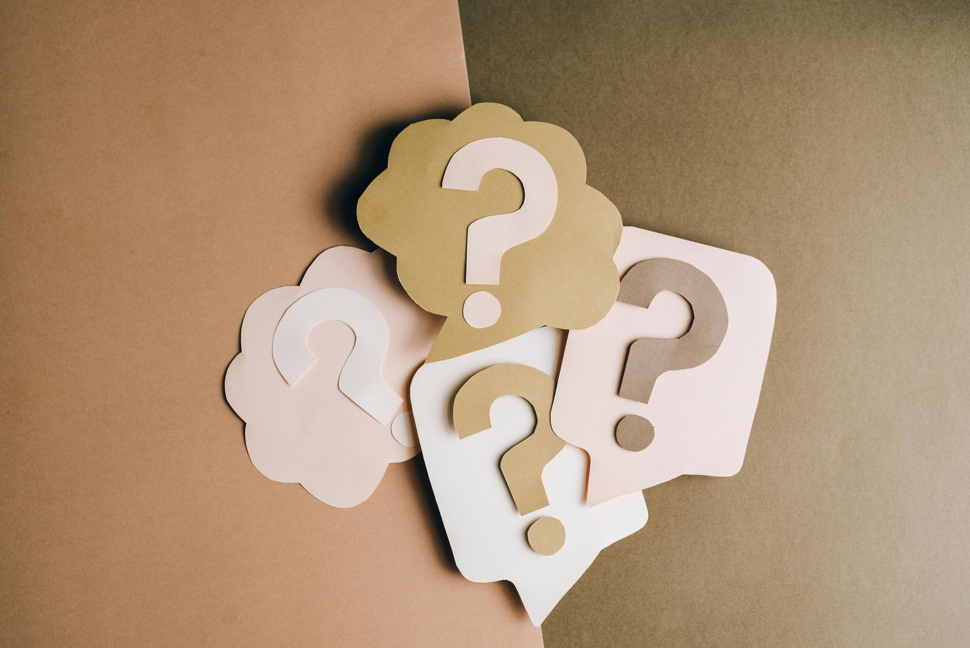 Paper cut out into question marks, set against contrasting cardboard speech bubble cutouts