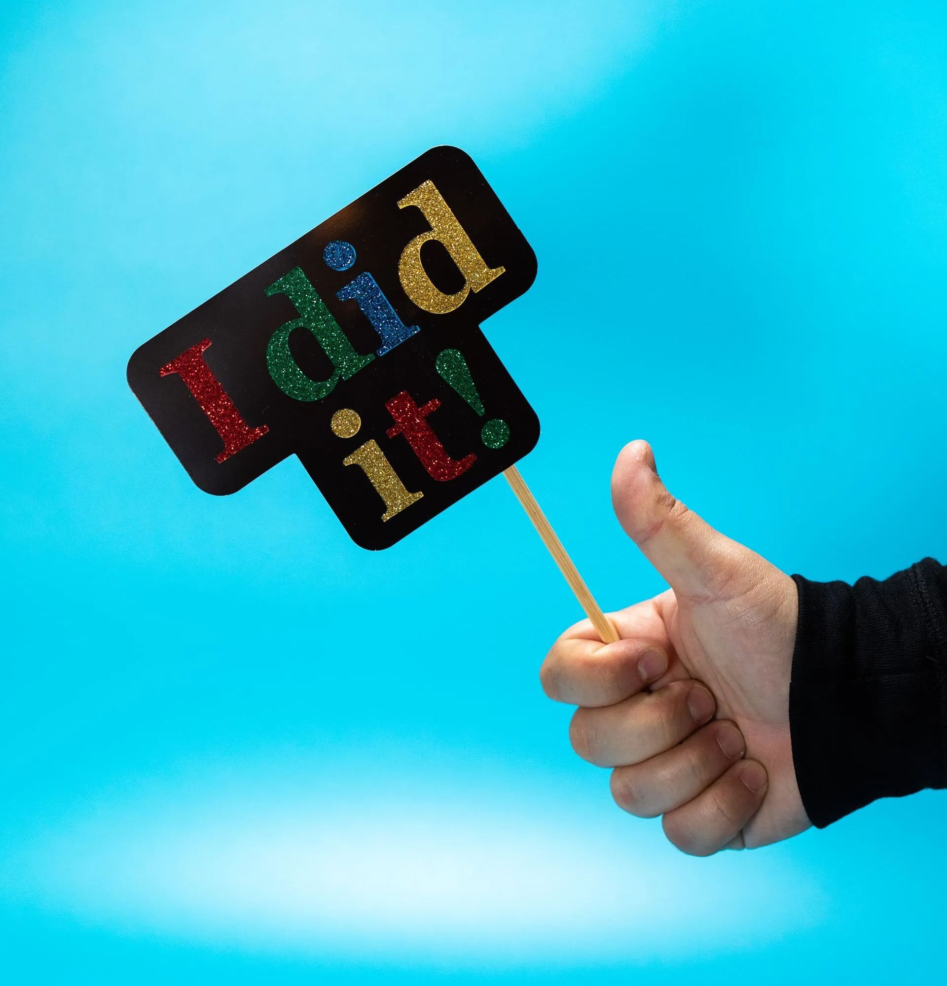 Blue background with hand holding an I did it! sign in red, green, blue and yellow sparkly writing.
