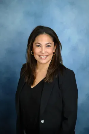 Smiling person in a black blazer against a blue studio backdrop