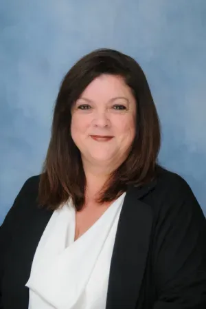 Portrait of a smiling woman in a black blazer against a blue studio backdrop