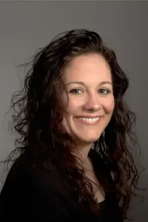 Smiling woman with long dark curly hair against a plain gray background
