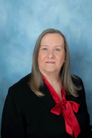 Portrait of a woman in a black top with a red bow against a blue studio backdrop