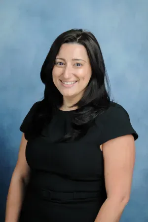 Smiling woman in a black dress posed against a blue studio backdrop