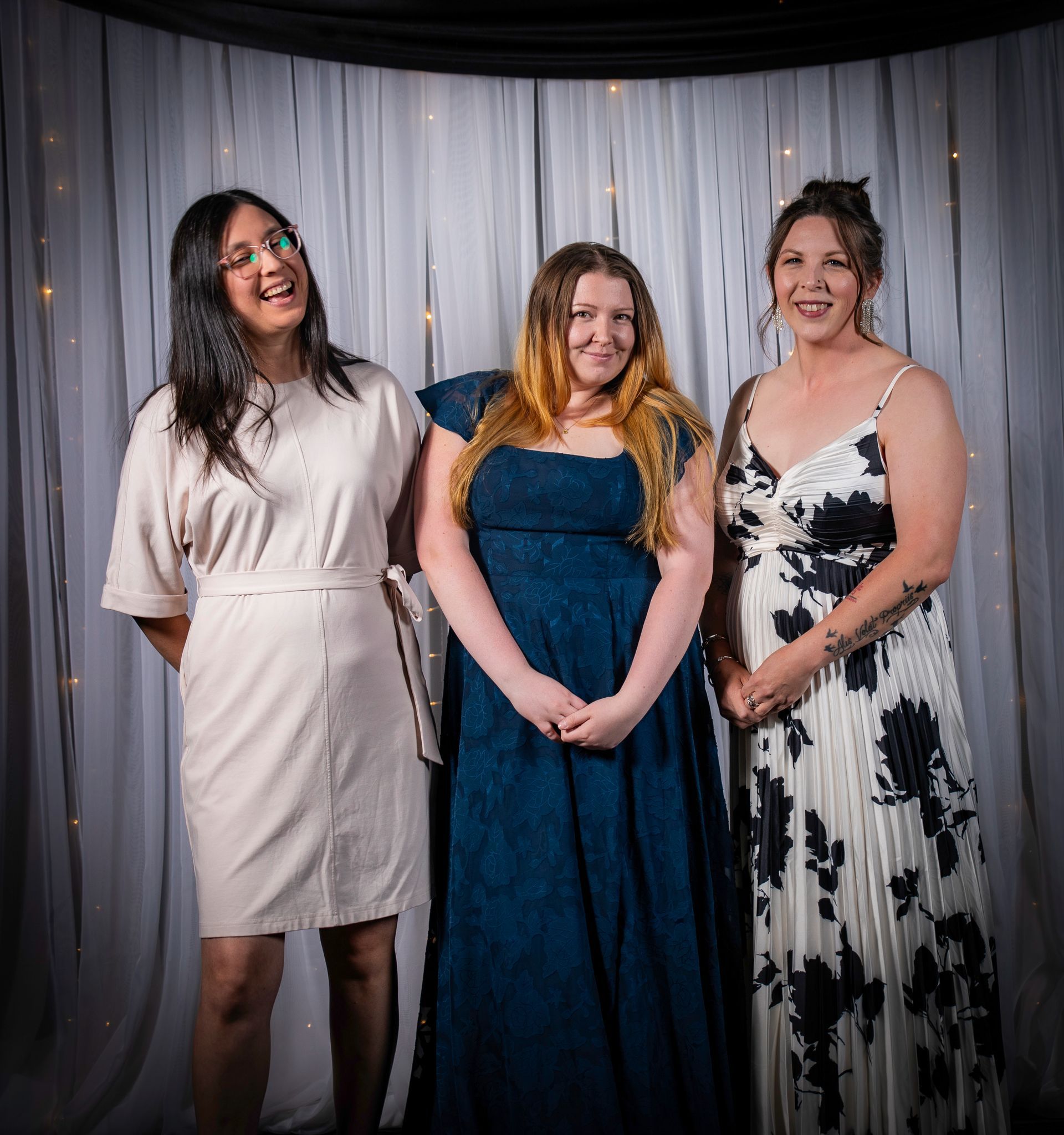 Three women smiling and posing in front of a draped white backdrop.
