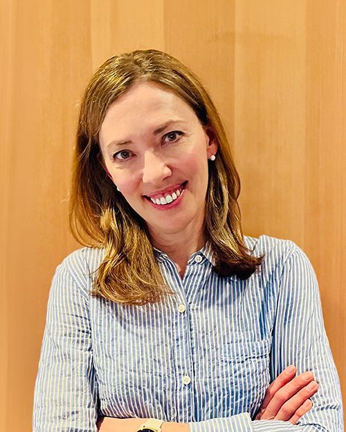Beckie Scott in a blue striped shirt with arms crossed against a wooden wall