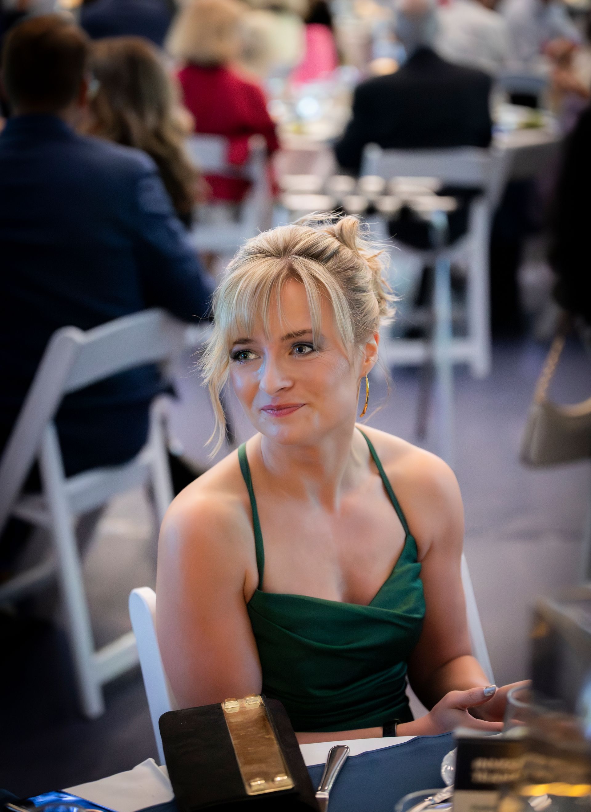 Blonde woman in a green dress seated at a table in a blurred event venue