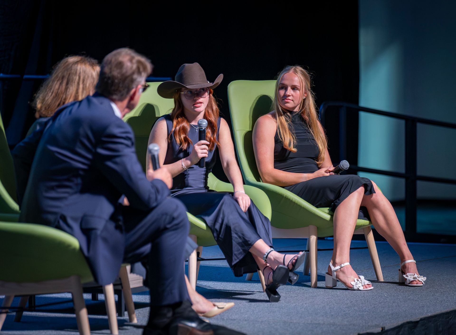 4 panelists seated on stage chairs during a discussion, with a moderator in the foreground.