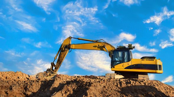Yellow excavator on a dirt mound under a blue sky with clouds