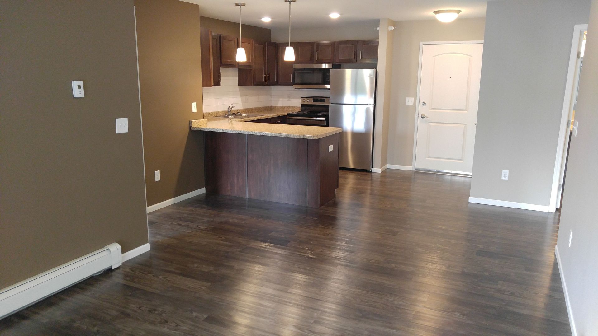 Open kitchen with brown cabinets, stainless steel appliances, and dark wood flooring.