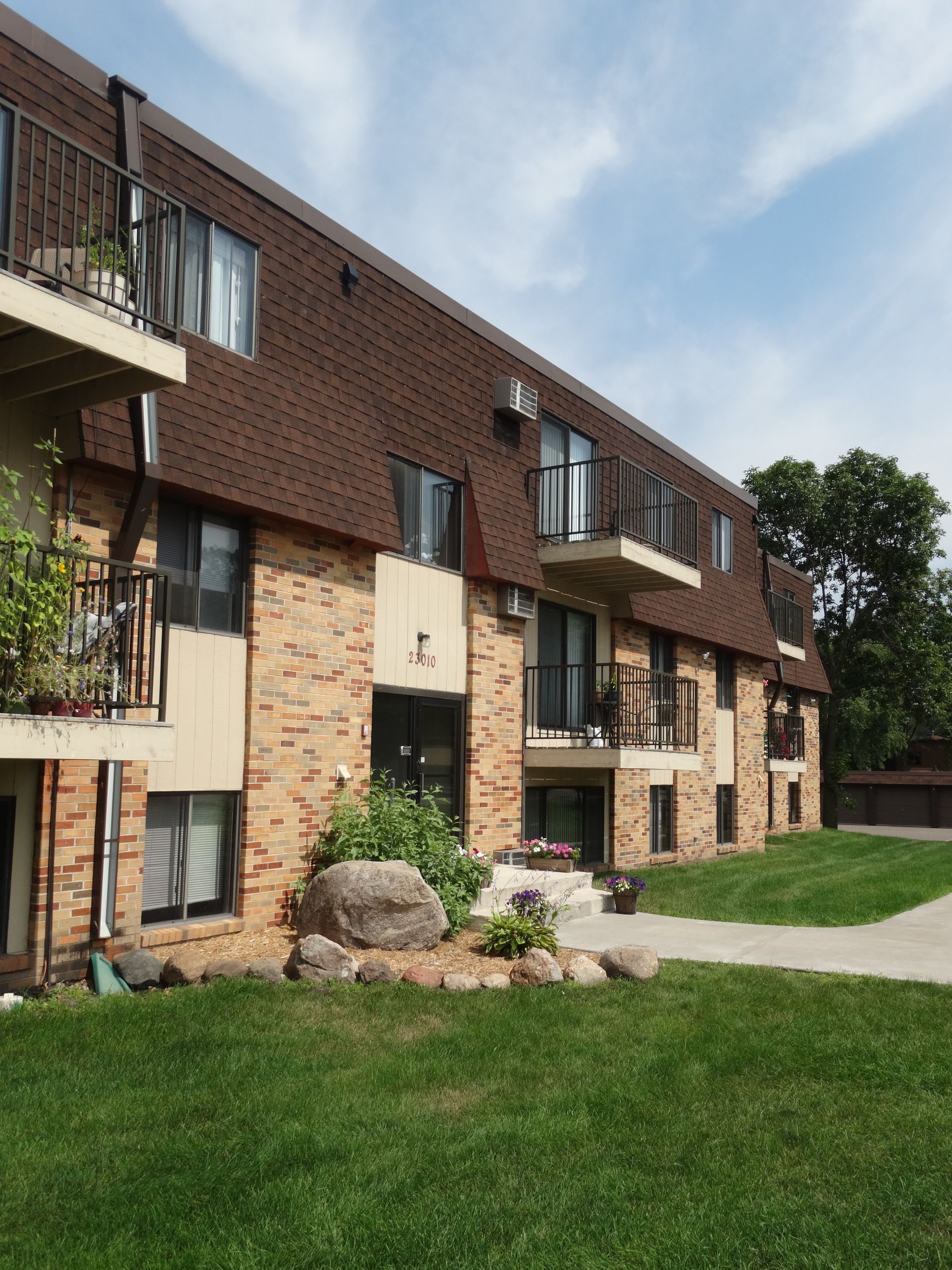 Apartment building with brown roof, brick facade, and balconies on a sunny day.