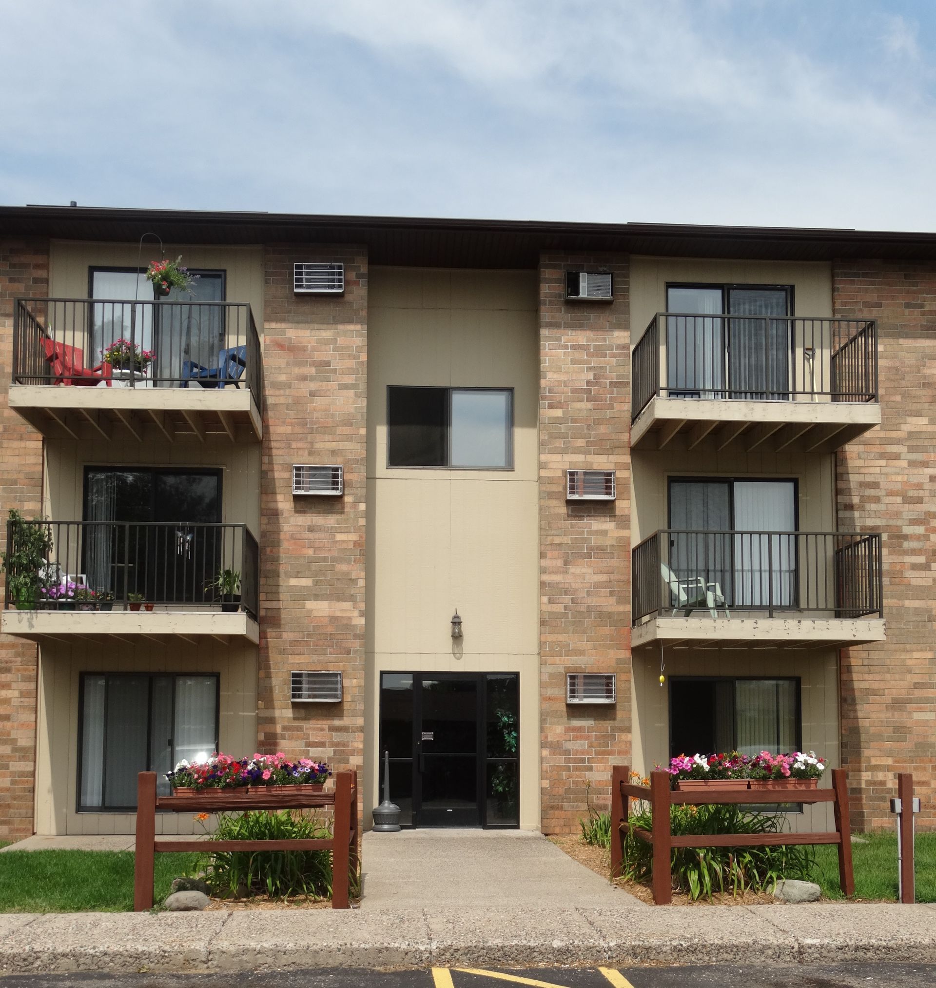 Apartment building with balconies, brown brick exterior, entrance, and flower boxes.