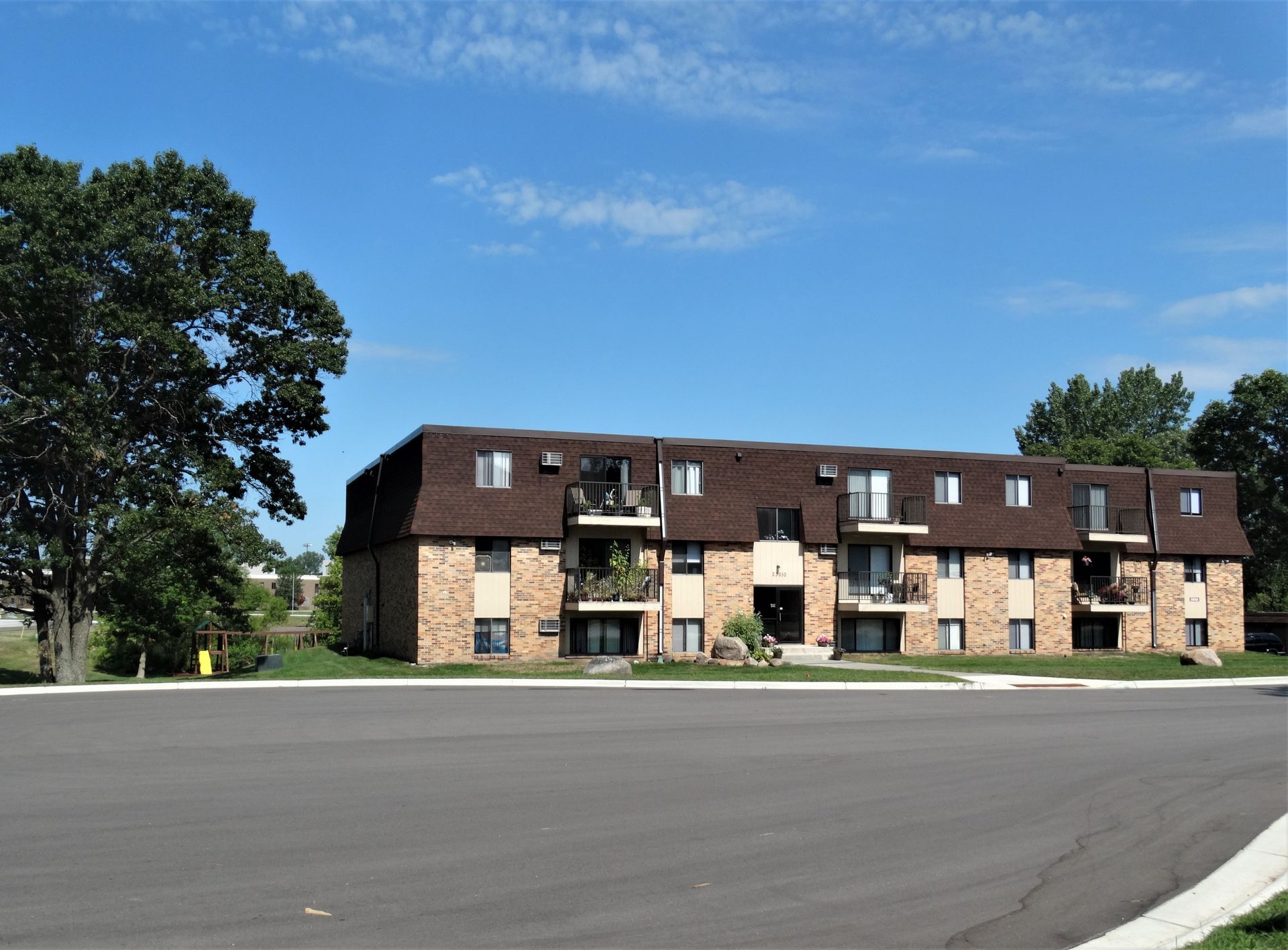 Apartment building with brown roof, beige brick, and balconies, on a sunny day with blue sky.