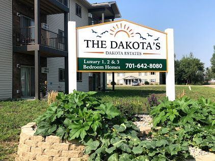 Sign for The Dakota's Dakota Estates apartments. White sign with green and gold text, showing a phone number and types of apartments.