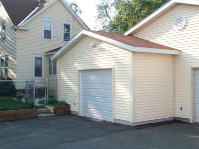 Beige house with a detached garage, asphalt driveway, and a chain-link fence on the left.
