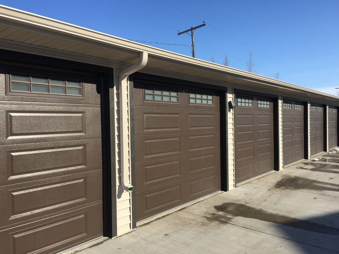 Brown garage doors in a row with windows, under a tan eave, against a blue sky.