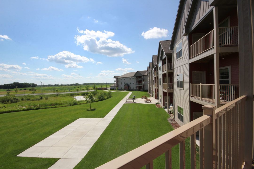 Balcony view of multi-story apartment buildings with green lawn and a small pond.