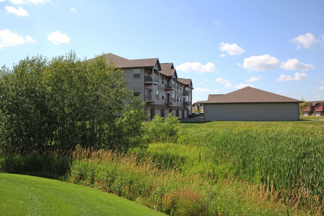 Apartment building in a field of tall grass and green vegetation under a blue sky with clouds.
