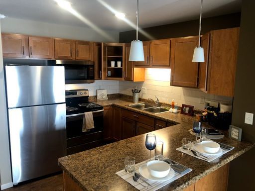 Kitchen with stainless steel appliances, wood cabinets, and a granite countertop with place settings.