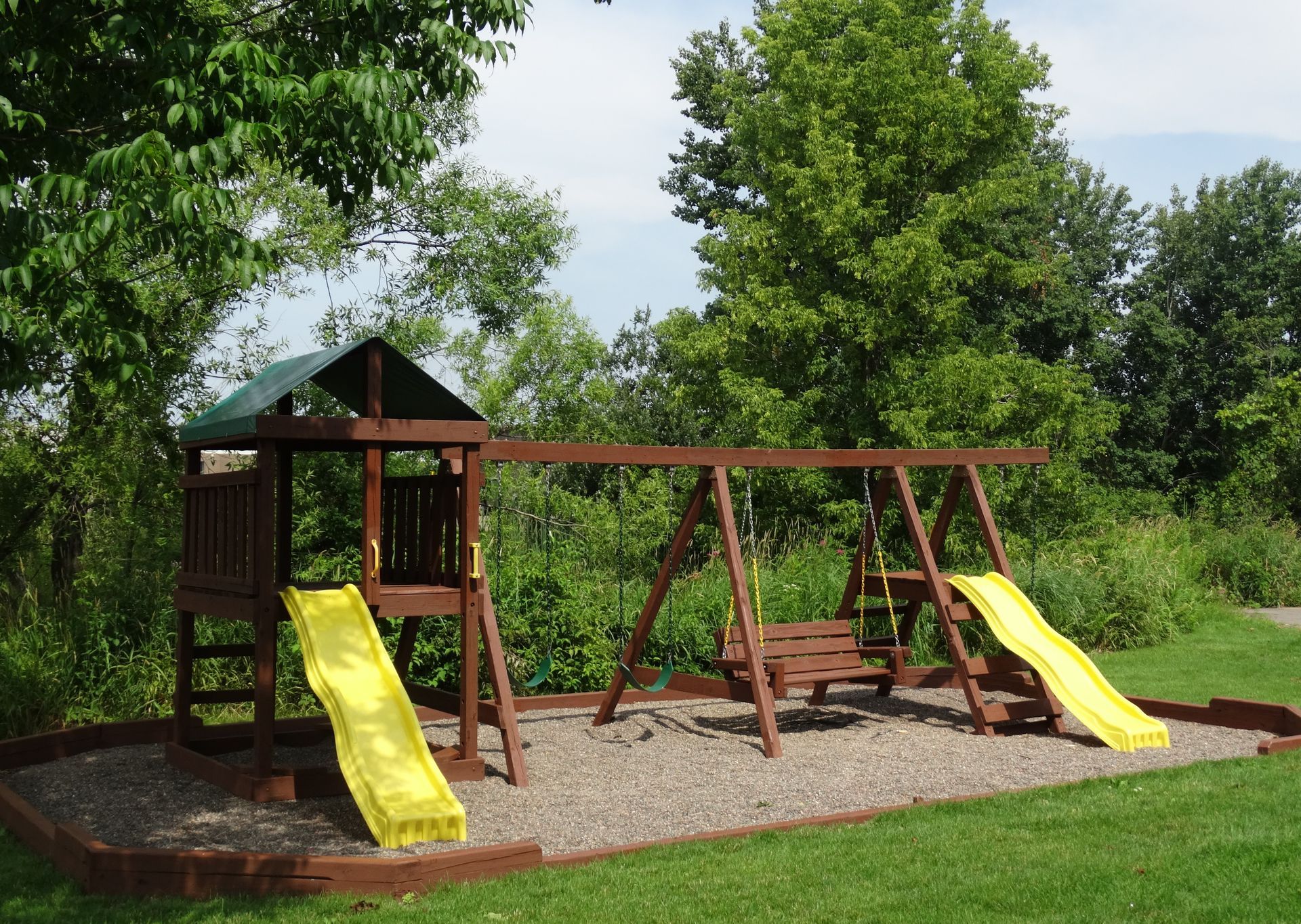 Wooden playground set with two slides and swings on a grassy area.