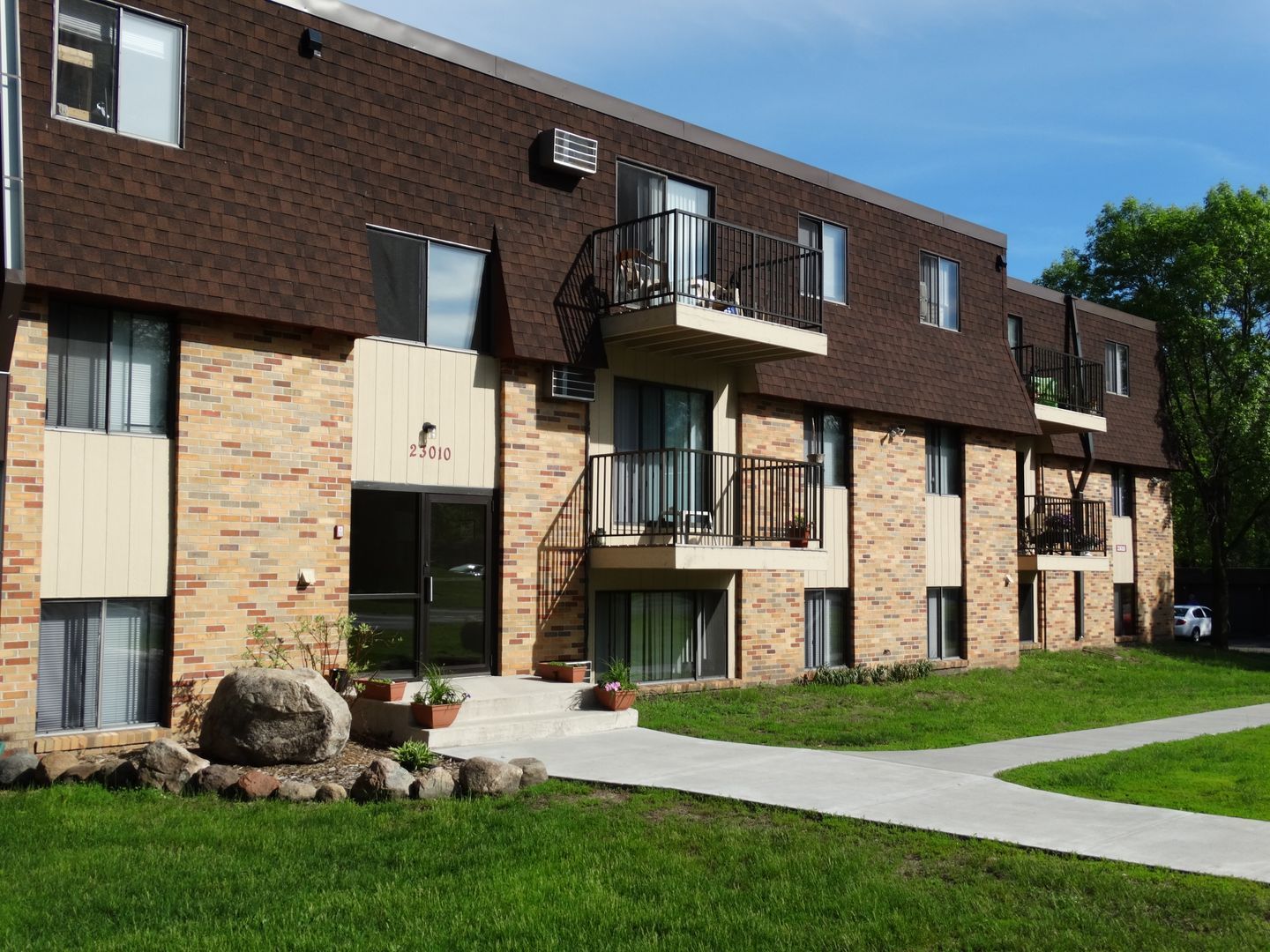 Apartment building with brown roof, brick facade, balconies, and green lawn.
