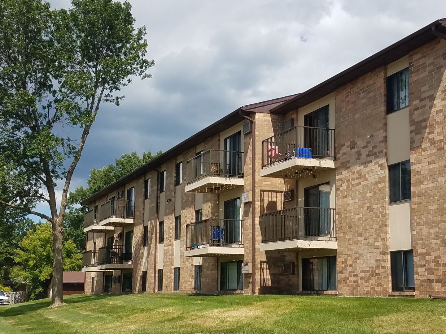 Apartment building with balconies; brick exterior, green grass, cloudy sky.