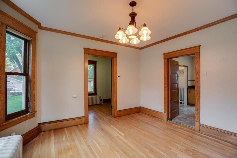 Empty room with wood floors, trim, and a chandelier. Open doorways lead to other rooms.