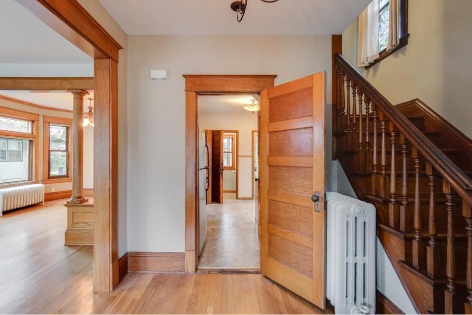 Entryway with wooden staircase, hardwood floors, and open doors to rooms with light-filled spaces.